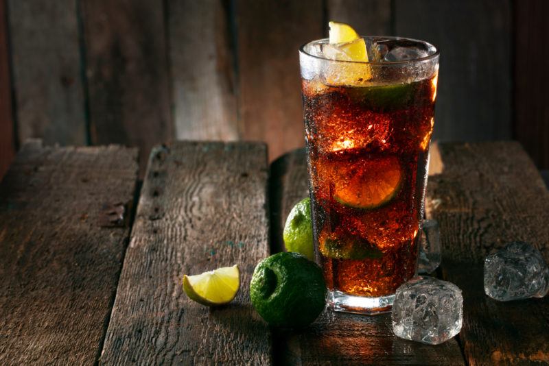 A rum and coke with ice and limes on a wooden table